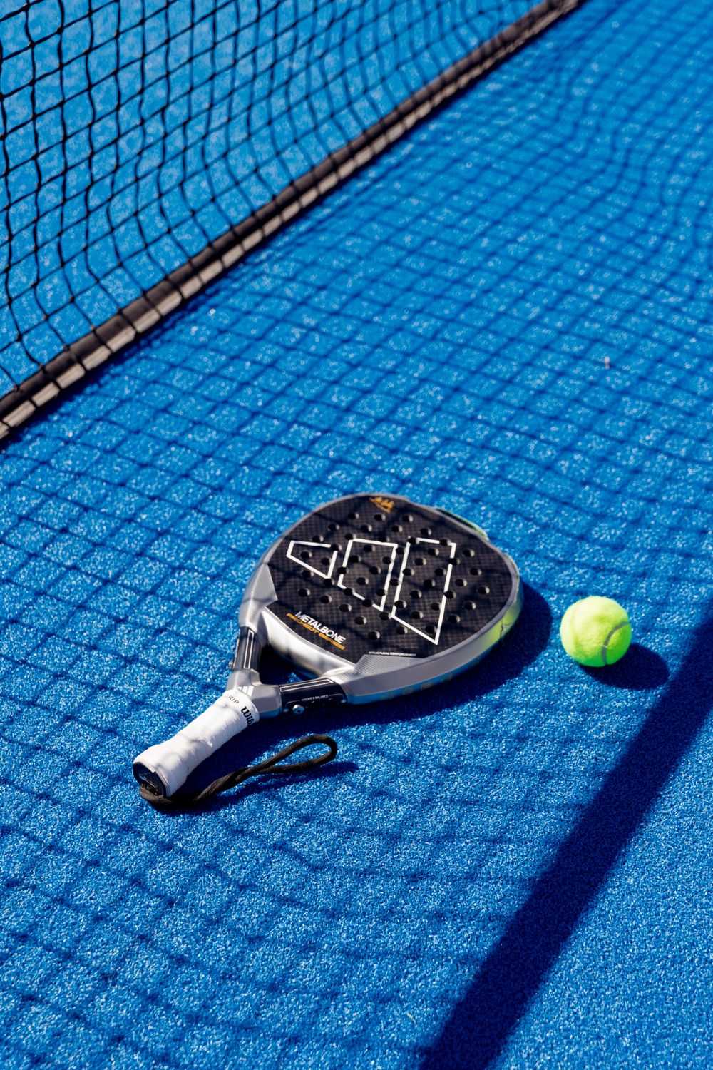 Pala de pádel y pelota sobre pista azul