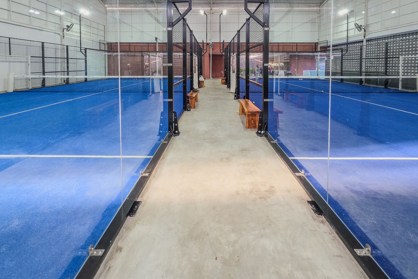 Complejo de pistas de pádel indoor vacías con suelo azul y paredes de cristal