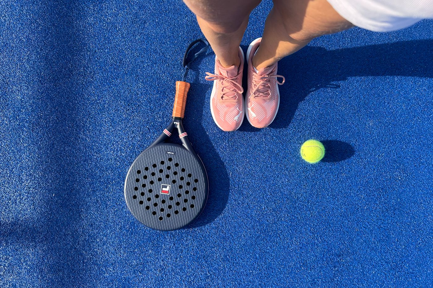 Vista cenital de una pala de pádel, zapatillas y pelota sobre una pista de pádel azul