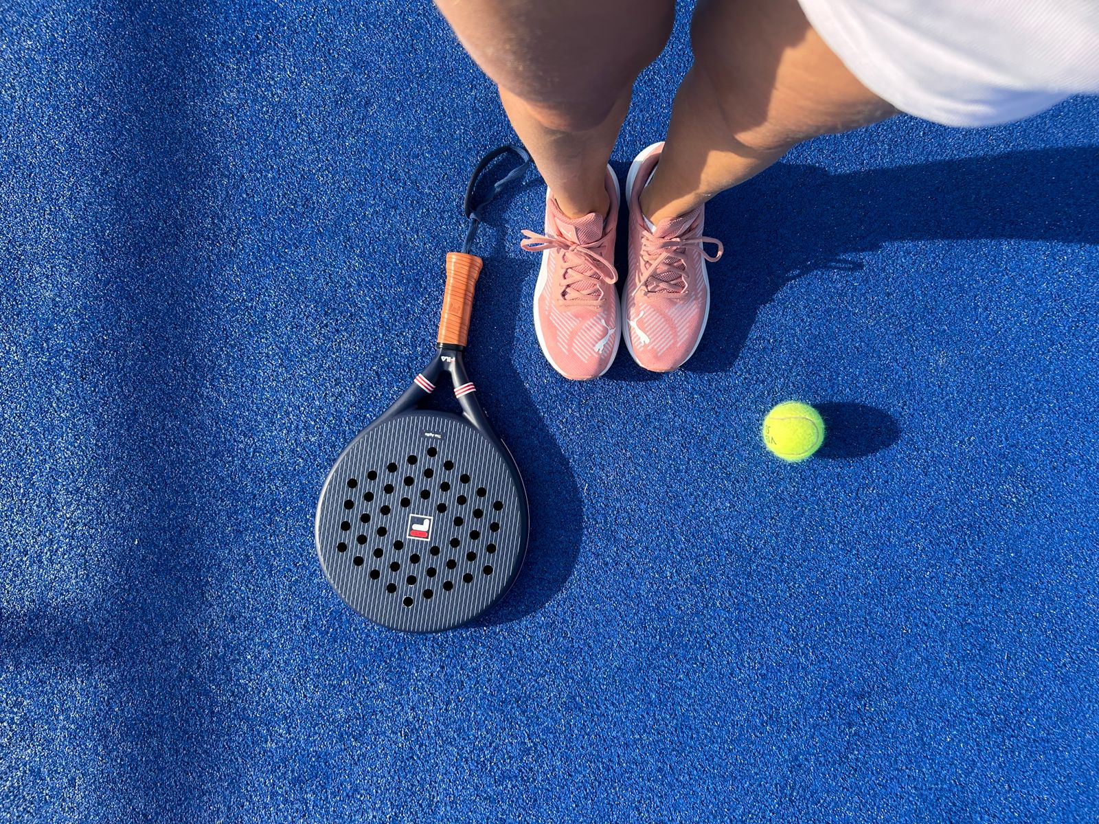 Zapatillas de pádel en pista azul con pala y pelota